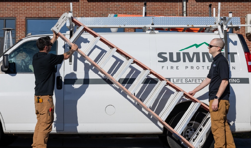 Workers handling a ladder near van.