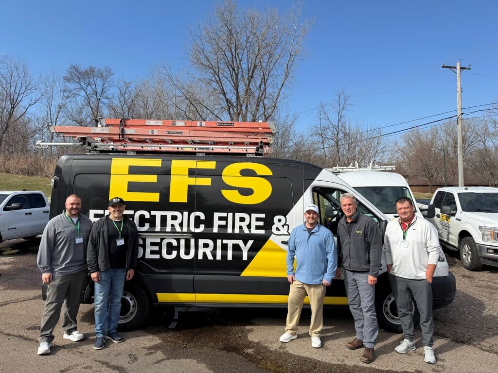 Five people standing next to an acquisition company truck