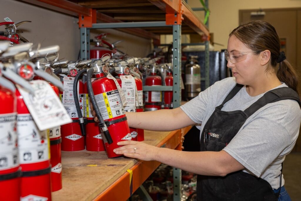 A Summit Fire Protection employee inspecting an ABC (multipurpose dry chemical) fire extinguisher