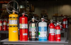 a row of various Summit Fire Protection portable fire extinguishers including a Class D, Class ABC, Restaurant, Water Mist, Carbon Dioxide, and Halotron extinguisher
