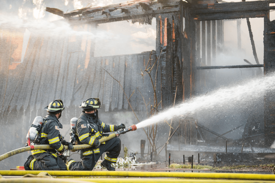 alt text: Fire fighters spray water into a burning building.)